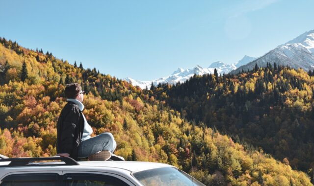 young woman, car, roof, sitting, mountains, sky, car wallpapers, nature, forest, spruce, pine, journey